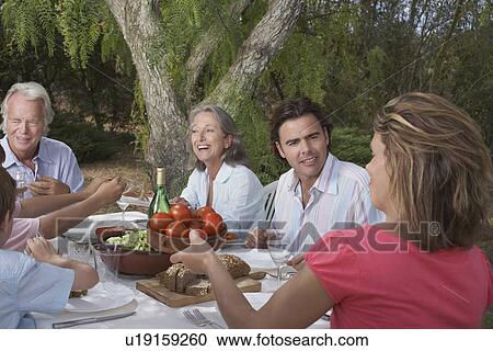 Stock Image - Three-generation family with children (6-11) dining in garden. Fotosearch