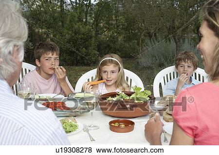 Stock Photo - Three-generation family with three children (6-11) sitting at table in garden. Fotosearch