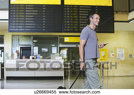 Traveller holding mobile phone in front of flight status board in airport View Large Photo Image Stock Photography - Traveller holding mobile phone in front of flight status board in airport. Fotosearch