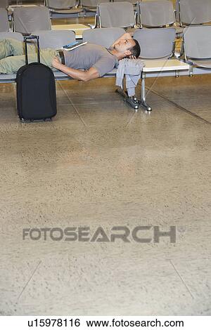 Stock Photograph - Traveller lying down on chairs in airport lobby. Fotosearch