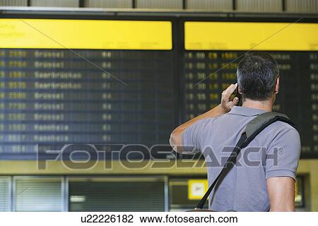 Traveller using mobile phone in front of flight status board in airport View Large Photo Image Stock Image - Traveller using mobile phone in front of flight status board in airport. Fotosearch