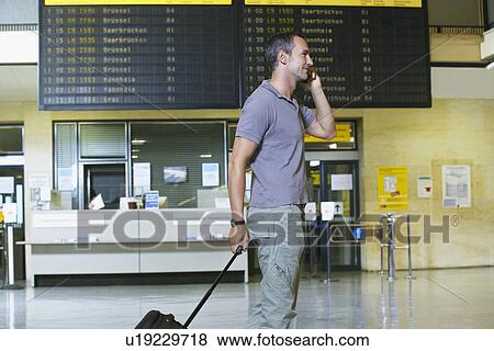 Traveller using mobile phone in front of flight status board in airport View Large Photo Image Stock Photo - Traveller using mobile phone in front of flight status board in airport. Fotosearch