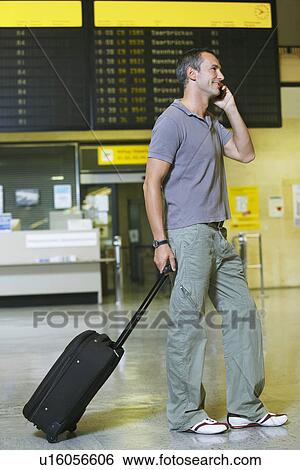 Stock Photograph - Traveller using mobile phone in front of flight status board in airport. Fotosearch