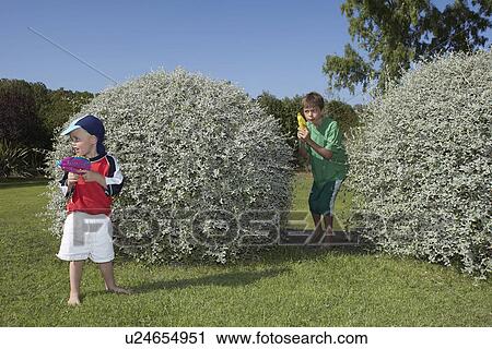 Two boys (3-11) playing with water pistols among bushes View Large Photo Image Stock Image - Two boys (3-11) playing with water pistols among bushes. Fotosearch