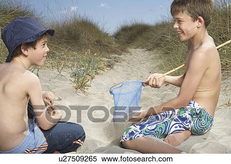 Stock Photography - Two boys (6-11) in sand dunes playing with fishing net. Fotosearch