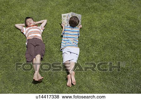 Stock Photo - Two boys (6-11) lying on grass one reading elevated view. Fotosearch