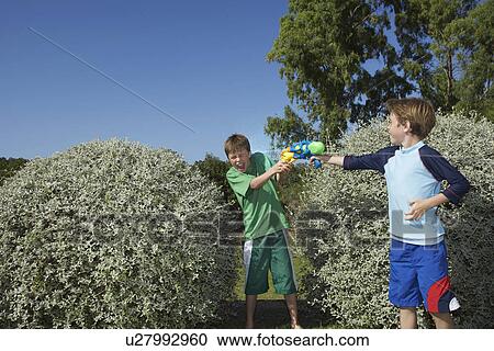Two boys (6-11) playing with water pistols among bushes laughing View Large Photo Image Stock Image - Two boys (6-11) playing with water pistols among bushes laughing. Fotosearch