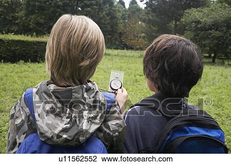 Stock Image - Two boys (7-9) with backpacks using compass back view. Fotosearch