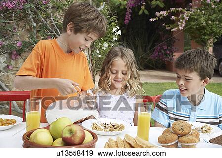 Two boys and girl (6-11) at table boy pouring milk on cereal garden View Large Photo Image Stock Photo - Two boys and girl (6-11) at table boy pouring milk on cereal garden. Fotosearch