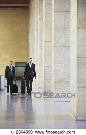 Two business men pulling luggage in airport lobby View Large Photo Image Stock Image - Two business men pulling luggage in airport lobby. Fotosearch