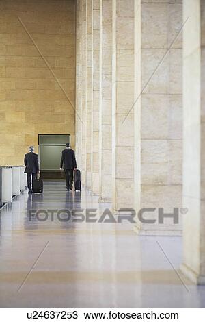 Two business men pulling luggage in airport lobby back view View Large Photo Image Stock Image - Two business men pulling luggage in airport lobby back view. Fotosearch