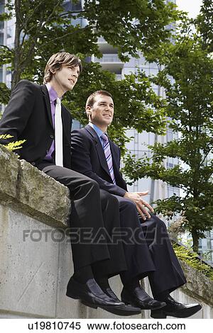Stock Photography - Two business men sitting on wall outdoors. Fotosearch
