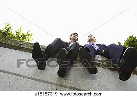 Two business men sitting side by side on wall low angle view View Large Photo Image Stock Photo - Two business men sitting side by side on wall low angle view. Fotosearch
