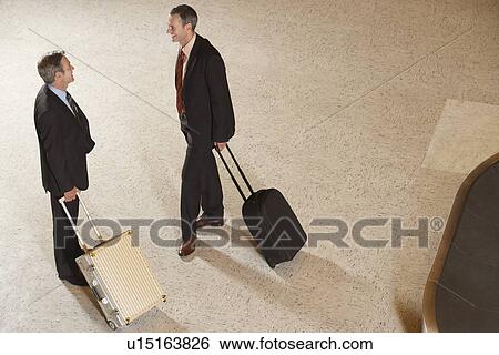 Two business men standing with suitcases by luggage carousel in airport View Large Photo Image Stock Photograph - Two business men standing with suitcases by luggage carousel in airport. Fotosearch