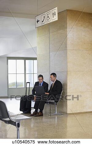 Stock Photography - Two business men using laptop in airport lobby. Fotosearch