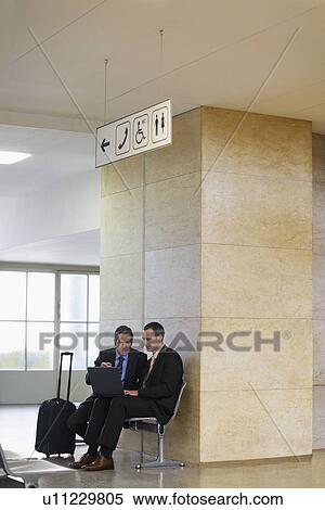 Two business men using laptop in airport lobby View Large Photo Image Stock Photography - Two business men using laptop in airport lobby. Fotosearch