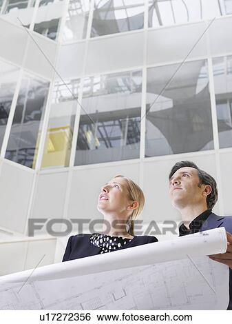 Two business people holding blueprint low angle view View Large Photo Image Stock Photograph - Two business people holding blueprint low angle view. Fotosearch