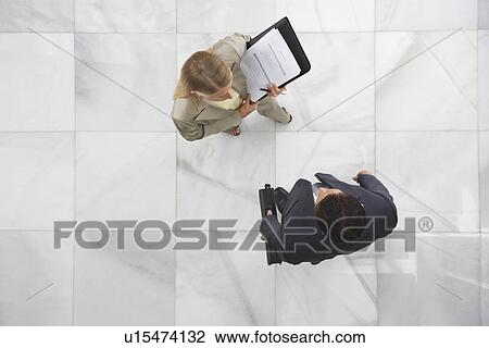 Stock Image - Two business people standing in lobby. Fotosearch