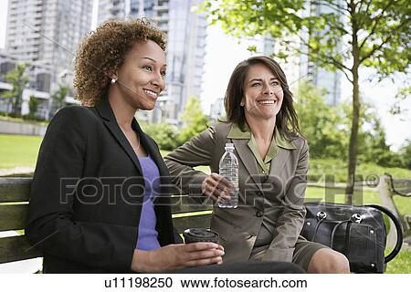 Two business women drinking on park bench View Large Photo Image Stock Image - Two business women drinking on park bench. Fotosearch