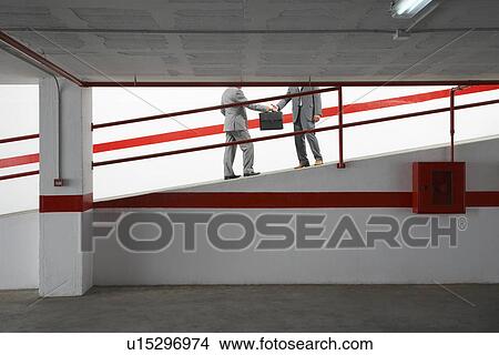 Two businessmen exchanging briefcase on ramp in parking garage View Large Photo Image Picture - Two businessmen exchanging briefcase on ramp in parking garage. Fotosearch