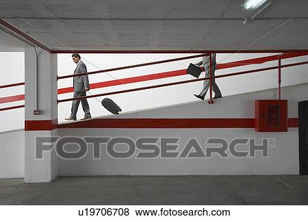 Two businessmen walking down ramp in parking garage with luggage View Large Photo Image Stock Photo - Two businessmen walking down ramp in parking garage with luggage. Fotosearch