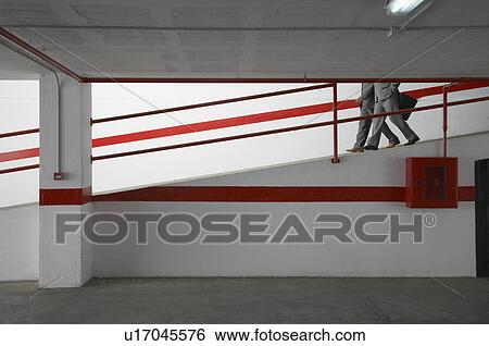 Two businessmen walking down ramp in parking garage View Large Photo Image Stock Photograph - Two businessmen walking down ramp in parking garage. Fotosearch