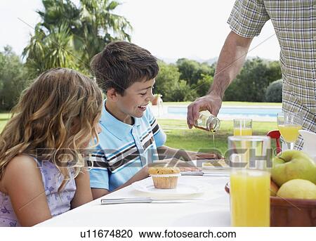 Stock Image - Two children at table (6-11) father pouring syrup. Fotosearch