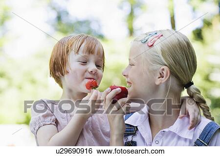 Two girls (3-7) eating fruits smiling View Large Photo Image Stock Photograph - Two girls (3-7) eating fruits smiling. Fotosearch
