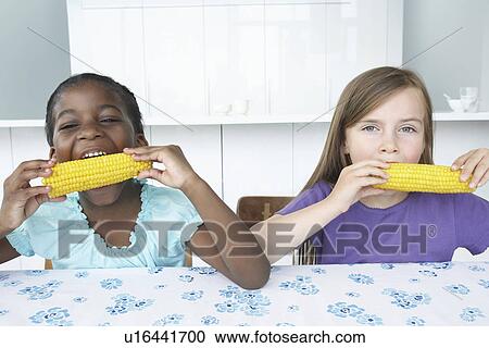 Two girls (5-6) sitting at table eating corn cobbs View Large Photo Image Stock Image - Two girls (5-6) sitting at table eating corn cobbs. Fotosearch