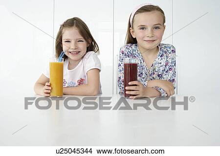 Picture - Two girls (7-9) sitting at table with orange and chocolate drinks portrait. Fotosearch