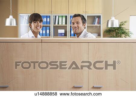 Two office workers smiling behind cubicle View Large Photo Image Stock Photo - Two office workers smiling behind cubicle. Fotosearch