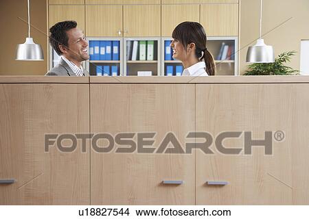 Picture - Two office workers talking behind cubicle. Fotosearch