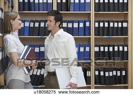 Stock Photography - Two office workers talking standing in file storage room. Fotosearch
