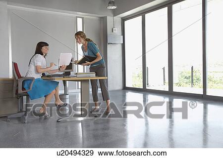 Stock Photo - Two women discussing document at desk in empty office building. Fotosearch