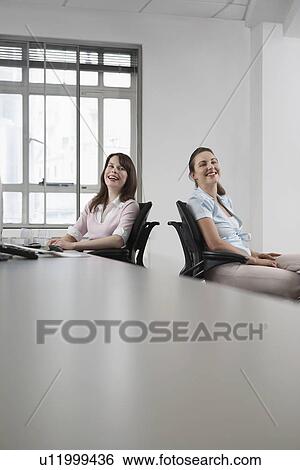 Stock Photograph - Two women sitting in office and laughing. Fotosearch