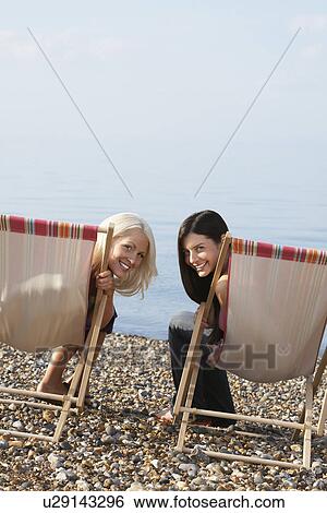 Two women sitting on deckchairs on beach portrait View Large Photo Image Stock Photograph - Two women sitting on deckchairs on beach portrait. Fotosearch