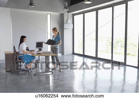 Two women talking at desk in empty office building View Large Photo Image Picture - Two women talking at desk in empty office building. Fotosearch