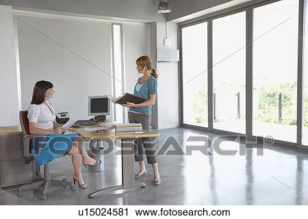 Two women talking at desk in empty office building View Large Photo Image Stock Image - Two women talking at desk in empty office building. Fotosearch