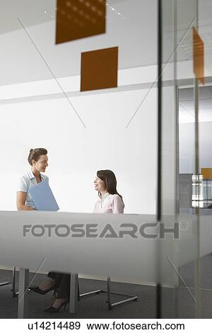 Stock Photo - Two women talking in office seen through glass. Fotosearch