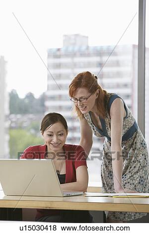Two women using laptop in office View Large Photo Image Stock Photo - Two women using laptop in office. Fotosearch
