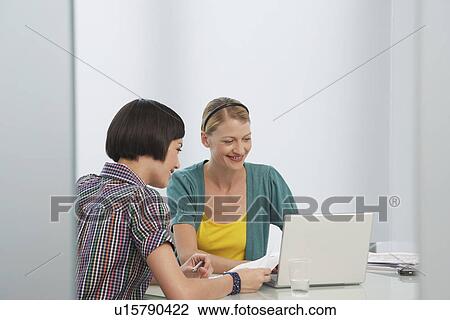 Two women working at laptop in office smiling View Large Photo Image Stock Image - Two women working at laptop in office smiling. Fotosearch