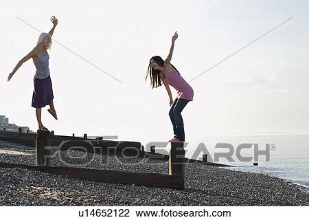 Two young women balancing on wooden wave breakers on beach View Large Photo Image Stock Image - Two young women balancing on wooden wave breakers on beach. Fotosearch