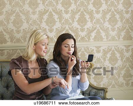 Two young women putting on make up sitting on sofa View Large Photo Image Stock Image - Two young women putting on make up sitting on sofa. Fotosearch
