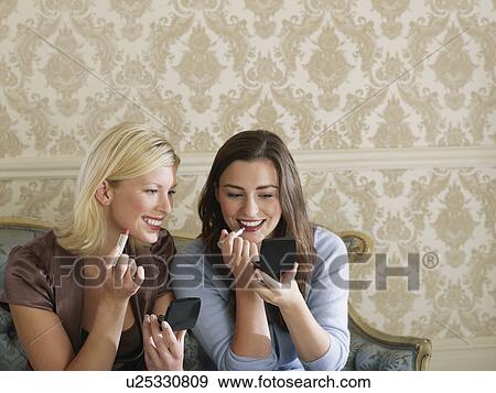 Two young women putting on make up sitting on sofa elevated view View Large Photo Image Stock Photo - Two young women putting on make up sitting on sofa elevated view. Fotosearch
