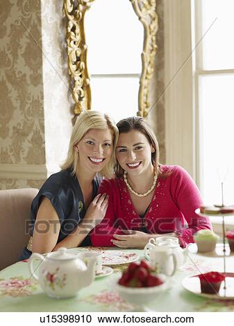 Stock Image - Two young women sitting at dining table portrait. Fotosearch