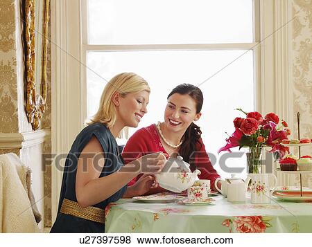 Two young women sitting at dining table pouring tea View Large Photo Image Stock Photo - Two young women sitting at dining table pouring tea. Fotosearch