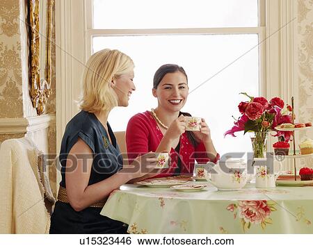 Two young women sitting at dining table drinking tea View Large Photo Image Stock Photograph - Two young women sitting at dining table drinking tea. Fotosearch