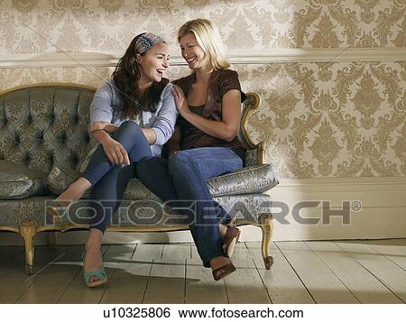 Stock Photograph - Two young women sitting on sofa laughing. Fotosearch