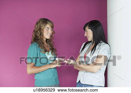 Two young women talking by purple wall View Large Photo Image Stock Photo - Two young women talking by purple wall. Fotosearch