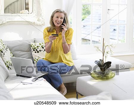 Stock Photo - Woman holding credit card using phone in living room elevated view. Fotosearch